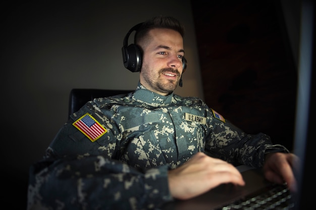 Free photo american soldier with headset in front of the laptop computer working in intelligence center