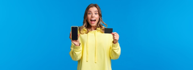 Free photo amused and excited blond girl recommend using banking service showing smartphone display and credit