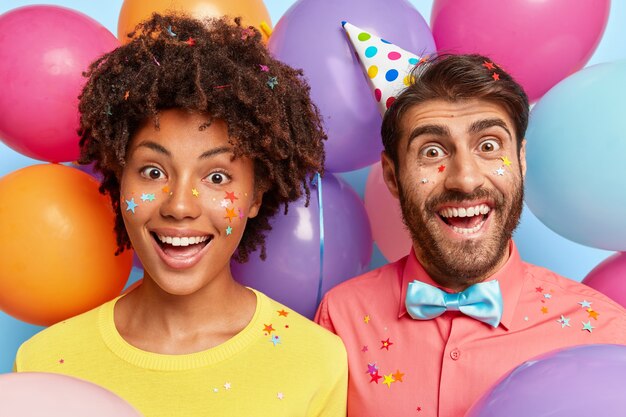 Amused joyful young couple posing surrounded by birthday colorful balloons