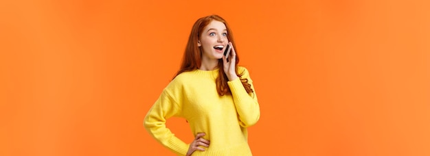 Amused and surprised smiling redhead girl widen eyes and look impressed as hear good news from frien