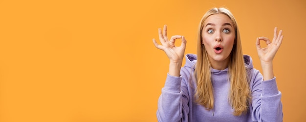 Free Photo amused talented creative young blond female tell excellent idea show okay no problem gesture persuade friends everything alright standing excited orange background ok signs folding lips amazed