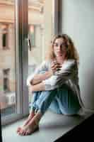 Free photo analog portrait of beautiful woman posing indoors on a windowsill