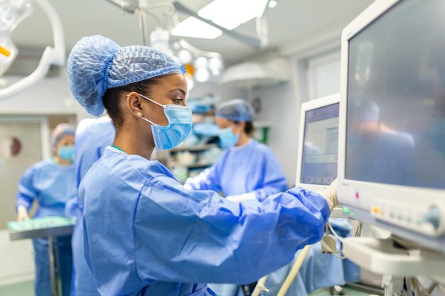 Anesthesiologist checking monitors while sedating patient before surgical procedure in hospital operating room Young adult female African American patient is asleep on operating table during surgery