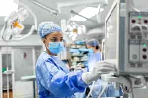 Free photo anesthetist working in operating theatre wearing protecive gear checking monitors while sedating patient before surgical procedure in hospital