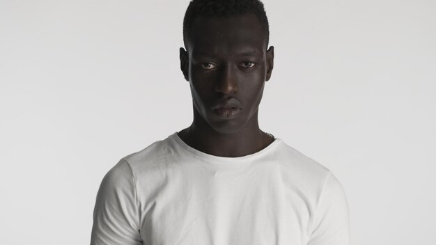 Angry African American guy wearing white tshirt looking aggressive on camera with over white background