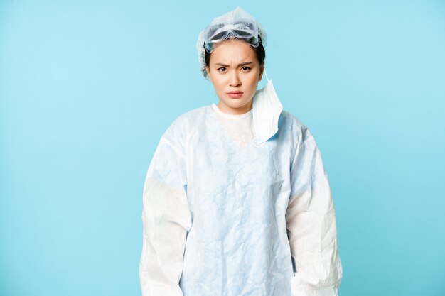 Angry asian woman doctor or nurse wearing personal protective equipment looking with disapproval fur...