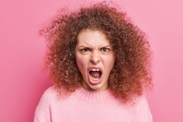 Angry disappointed young woman loses temper yells outraged keeps mouth wide opened expresses fury irritation or annoyance being fed up and pressured isolated over pink wall. I hate this