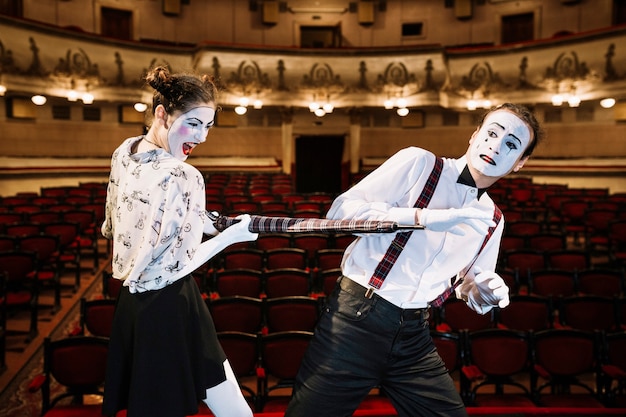 Free photo an angry female mime artist hitting male mime with an umbrella in the auditorium