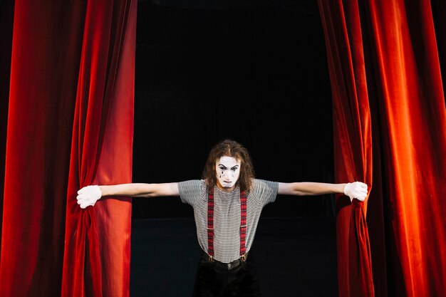 Angry male mime artist holding red curtain