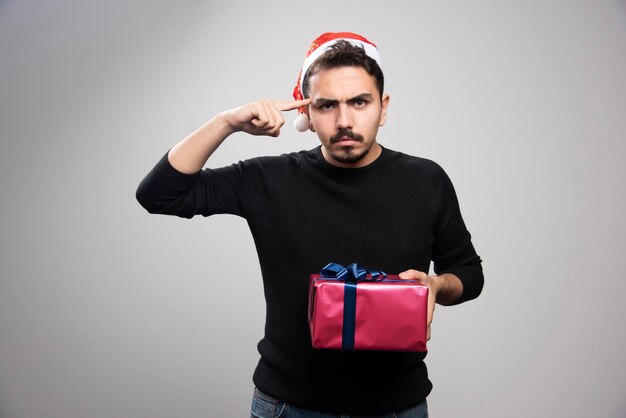 Angry man holding a gift box over a gray wall.