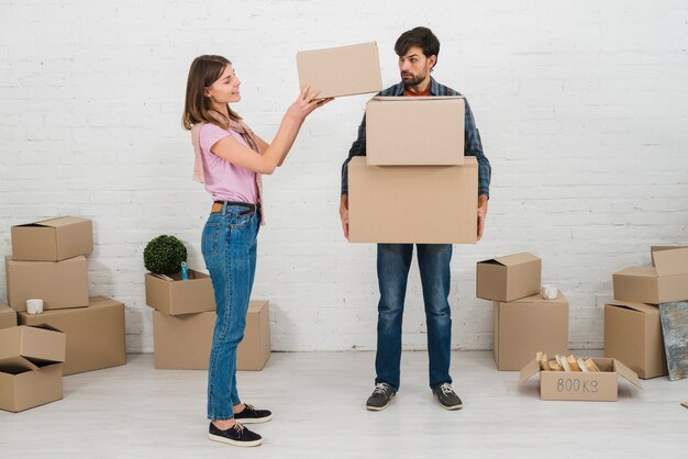 Angry man looking at her wife stacking the cardboard boxes over his hands