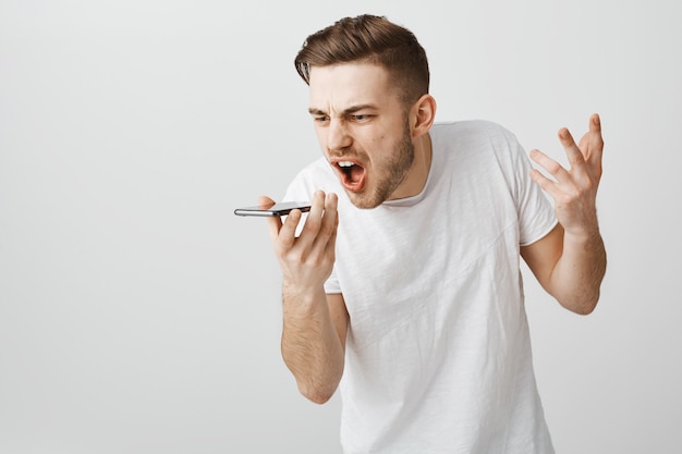 Angry pissed-off guy yelling at mobile speaker, record furious voice message