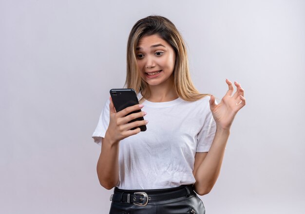 An angry pretty young woman in white t-shirt looking at mobile phone