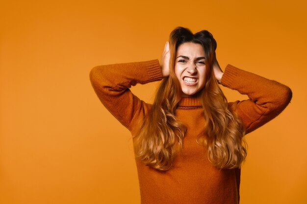 Angry redhead caucasian woman dressed in pullover with hands on her head