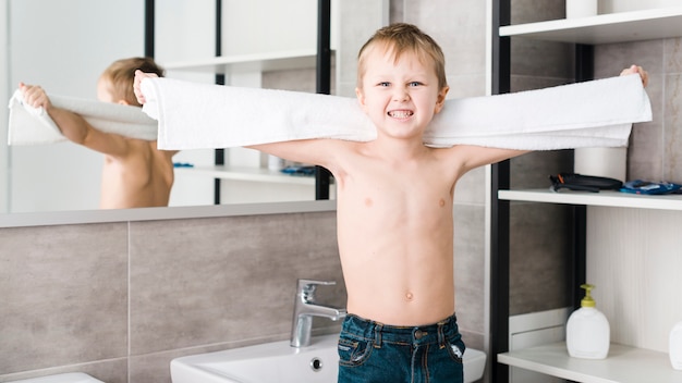 An angry shirtless boy holding towel in hand clenching his teeth at camera in the bathroom