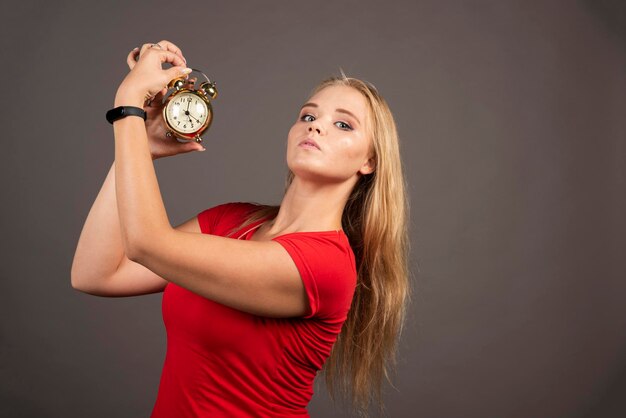 Angry woman posing with clock on dark background. High quality photo