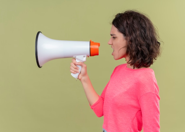 Angry young beautiful woman talking by speaker standing in profile view on isolated green wall