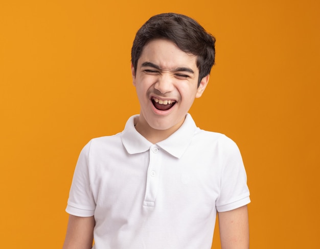 Angry young boy screaming with closed eyes isolated on orange wall