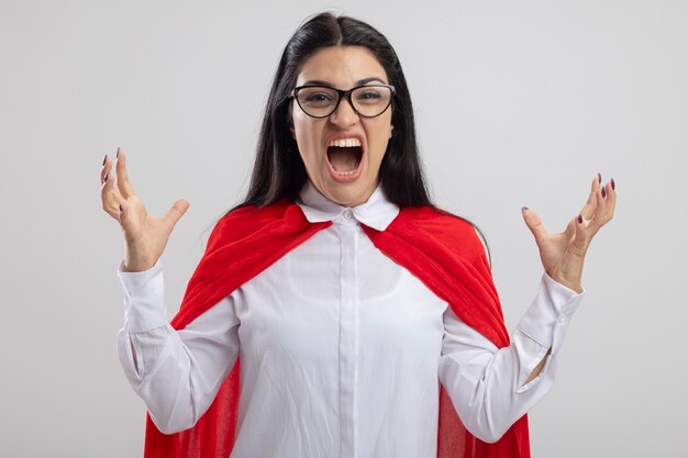 Angry young caucasian superhero girl wearing glasses keeping hands in air looking at camera and screaming isolated on white background