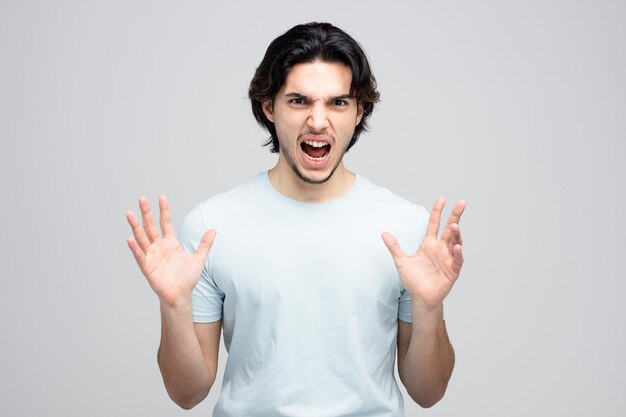 Angry young handsome man keeping hands in air looking at camera screaming isolated on white background