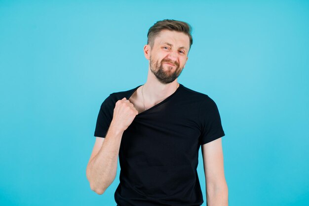 Angry young man is holding his shirt on blue background