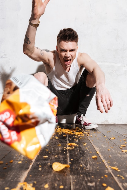 Angry young man throwing packet of potato chips in camera