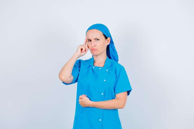 Angry young nurse is thinking by holding forefinger on temple on white background