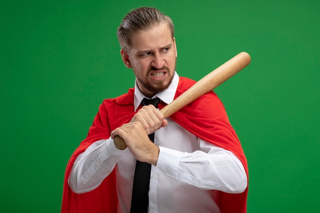 Free Photo angry young superhero guy and putting basebale bat on shoulder isolated on green