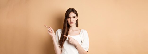 Angry young woman frowning pointing fingers right and complaining disappointed with logo standing up