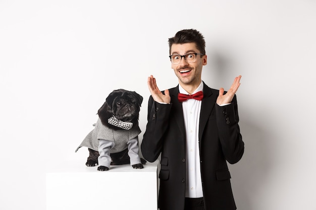 Animals, party and celebration concept. Handsome man and cute dog in costumes suits staring surprised at camera, reacting on promo offer amazed, white background