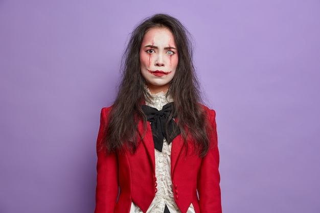 Free Photo annoyed displeased brunette woman has image of scary monster celebrates october festival and halloween wears professional spooky makeup poses against purple wall