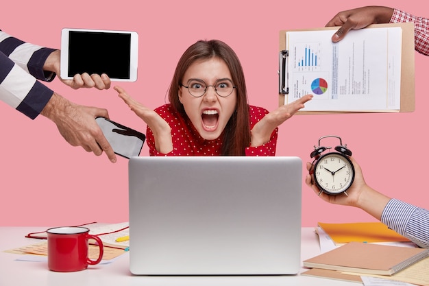 Free Photo annoyed freelancer gestures in front of laptop computer, has much paperwork, works overtime, cries desperately