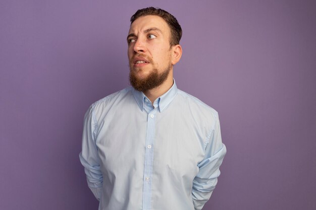 Annoyed handsome blonde man looks at side isolated on purple wall