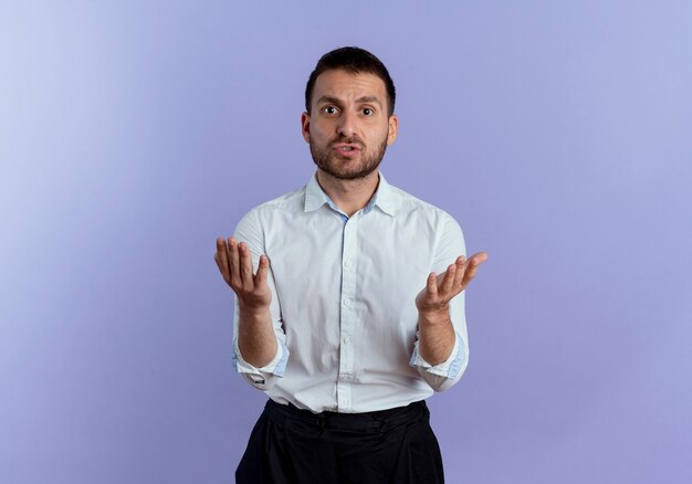 Annoyed handsome man holds hands looking isolated on purple wall