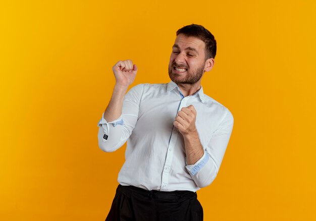 Annoyed handsome man stands with raised fists isolated on orange wall