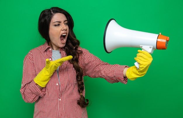 Annoyed pretty caucasian cleaner woman with rubber gloves holding and looking at loud speaker keeping hand open 