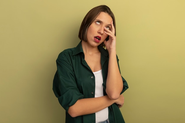 Annoyed pretty caucasian woman rolls eyes and puts hands on face on olive green