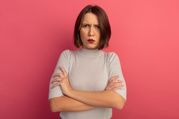 Annoyed pretty caucasian woman stands with crossed arms on pink