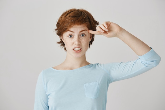 Annoyed redhead girl posing against the white wall