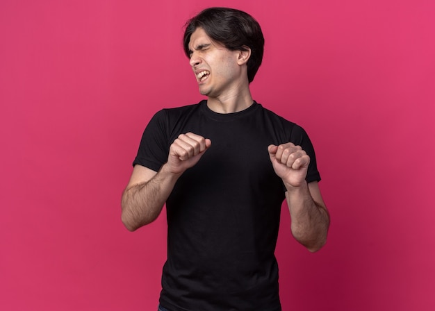 Free Photo annoyed with closed eyes young handsome guy wearing black t-shirt holding fists isolated on pink wall