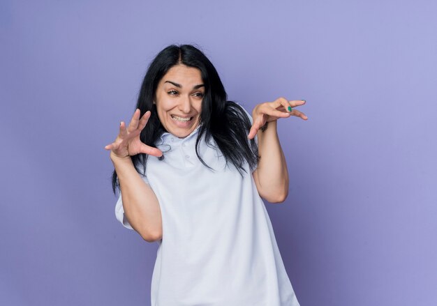 Annoyed young brunette caucasian girl squeezes hands looking at side isolated on purple wall