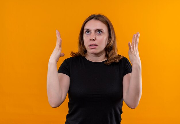 Annoyed young casual woman raising hands looking up on isolated orange space with copy space