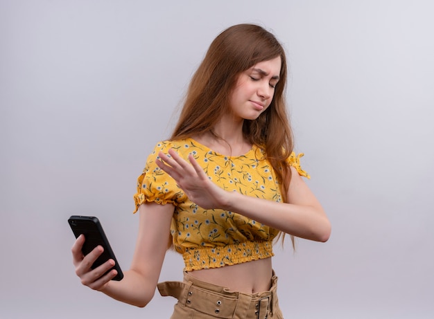 Annoyed young girl holding mobile phone and pointing with hand at mobile phone with closed eyes 