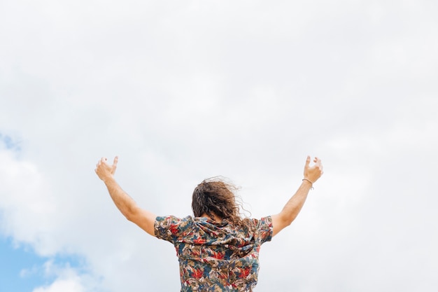 Free photo anonymous male rising hands to cloudy sky