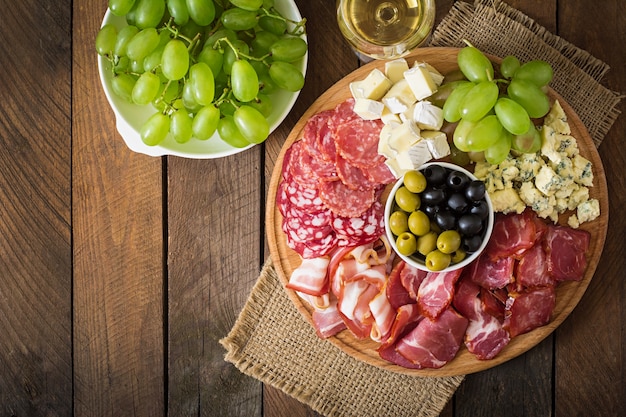 Free photo antipasto catering platter with bacon, jerky, salami, cheese and grapes on a wooden table