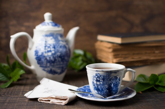 Antique porcelain tea cup and teapot with books and folded napkin on wooden table