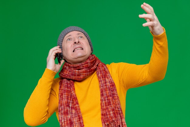 Anxious adult man with winter hat and scarf around his neck talking on phone looking up 