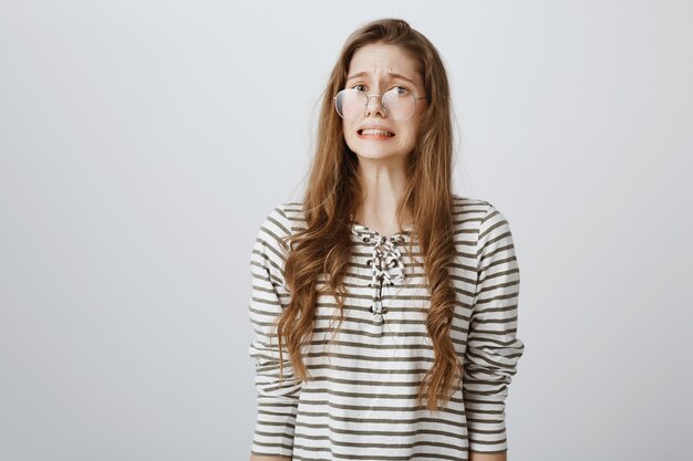 Anxious cute girl in glasses looking awkward and scared