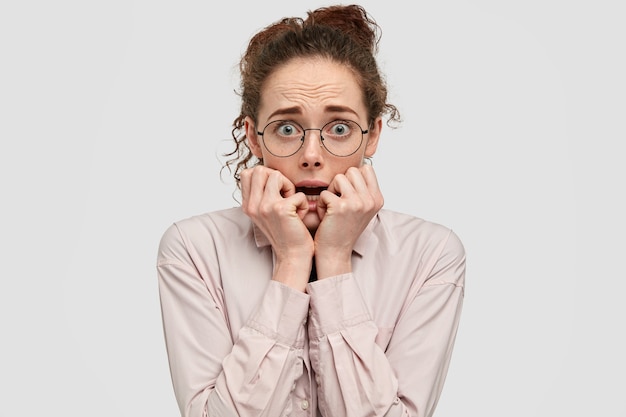 Free photo anxious freckled girl looks nervously at camera, stares in distrust, bites finger nails