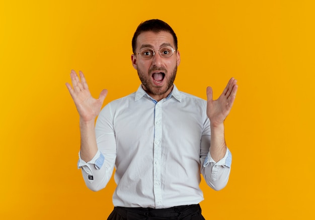 Anxious handsome man with optical glasses raises hands isolated on orange wall